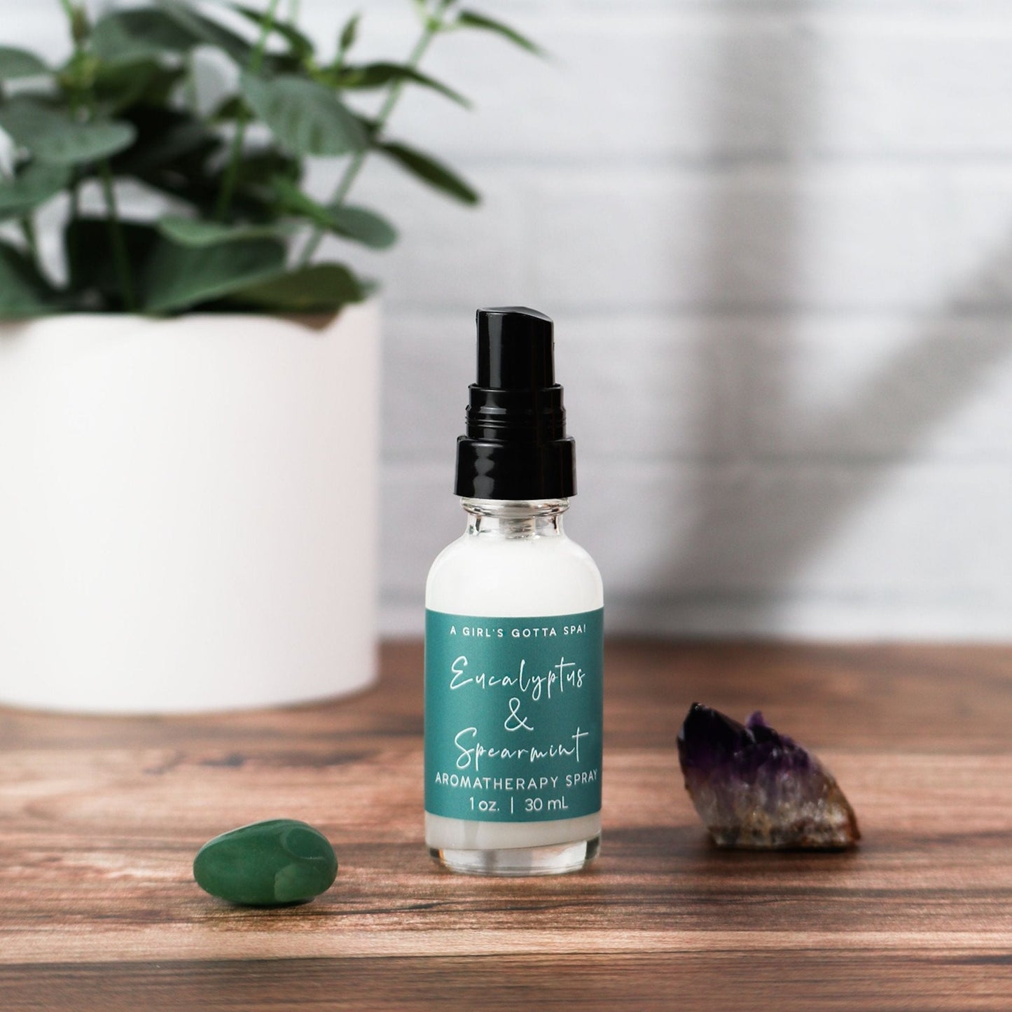 Aromatherapy spray bottle on a wooden surface with a plant and crystals in the background