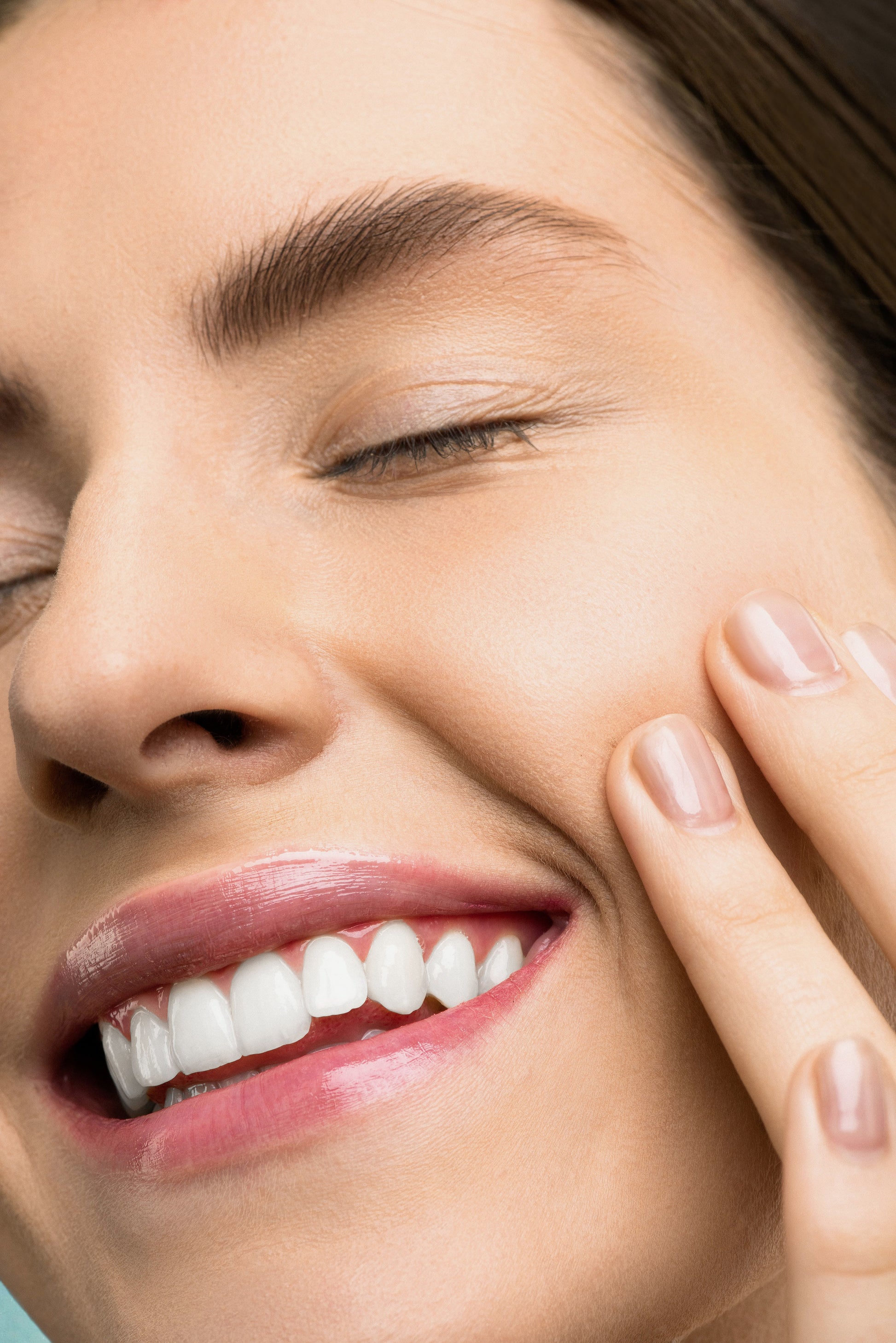 Close-up of a woman's face with a focus on her smile and hand near her face.