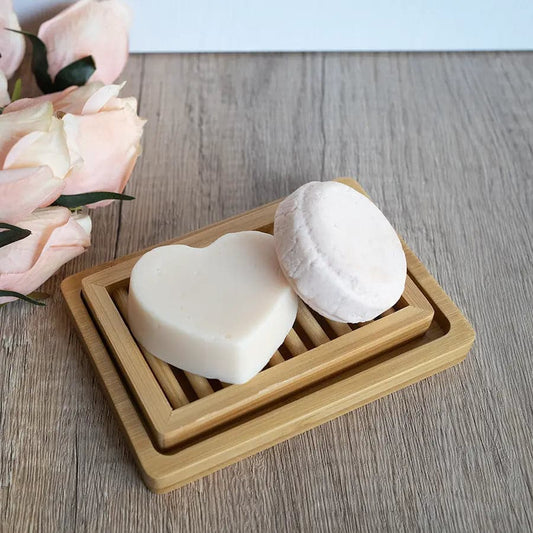 Two heart-shaped soaps on a wooden soap dish with flowers in the background.
