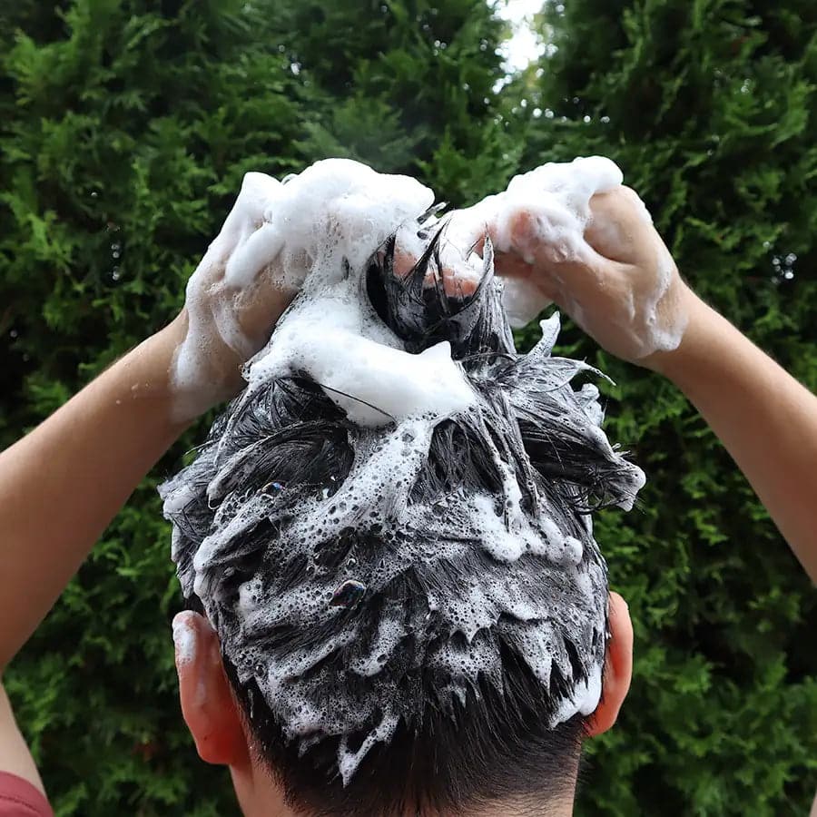 Person washing their hair with soapy water outdoors